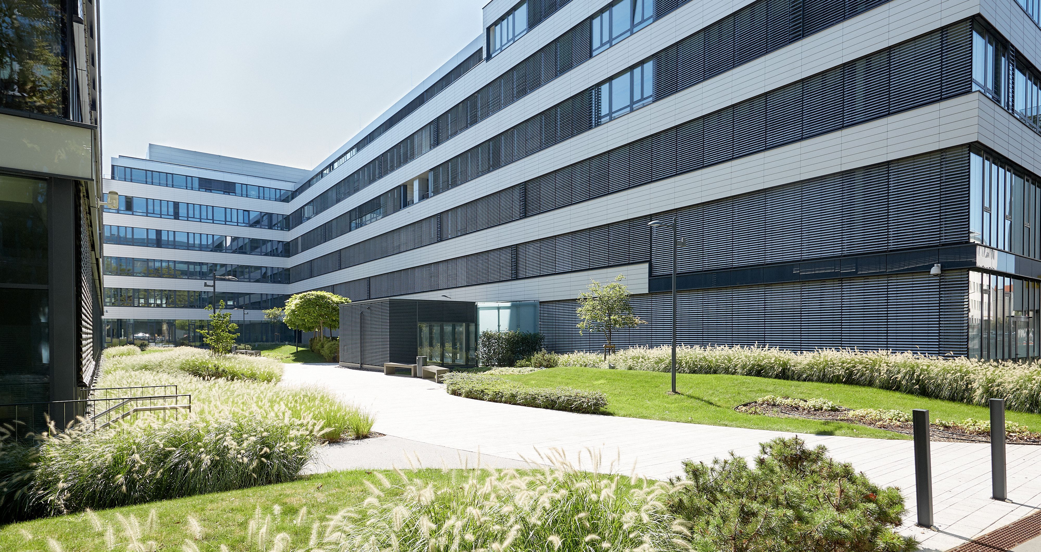Foto: Innenhof zwischen hochmodernen Bürogebäuden mit Alu-Glas-Fassaden und modern gestalteten Grünflächen