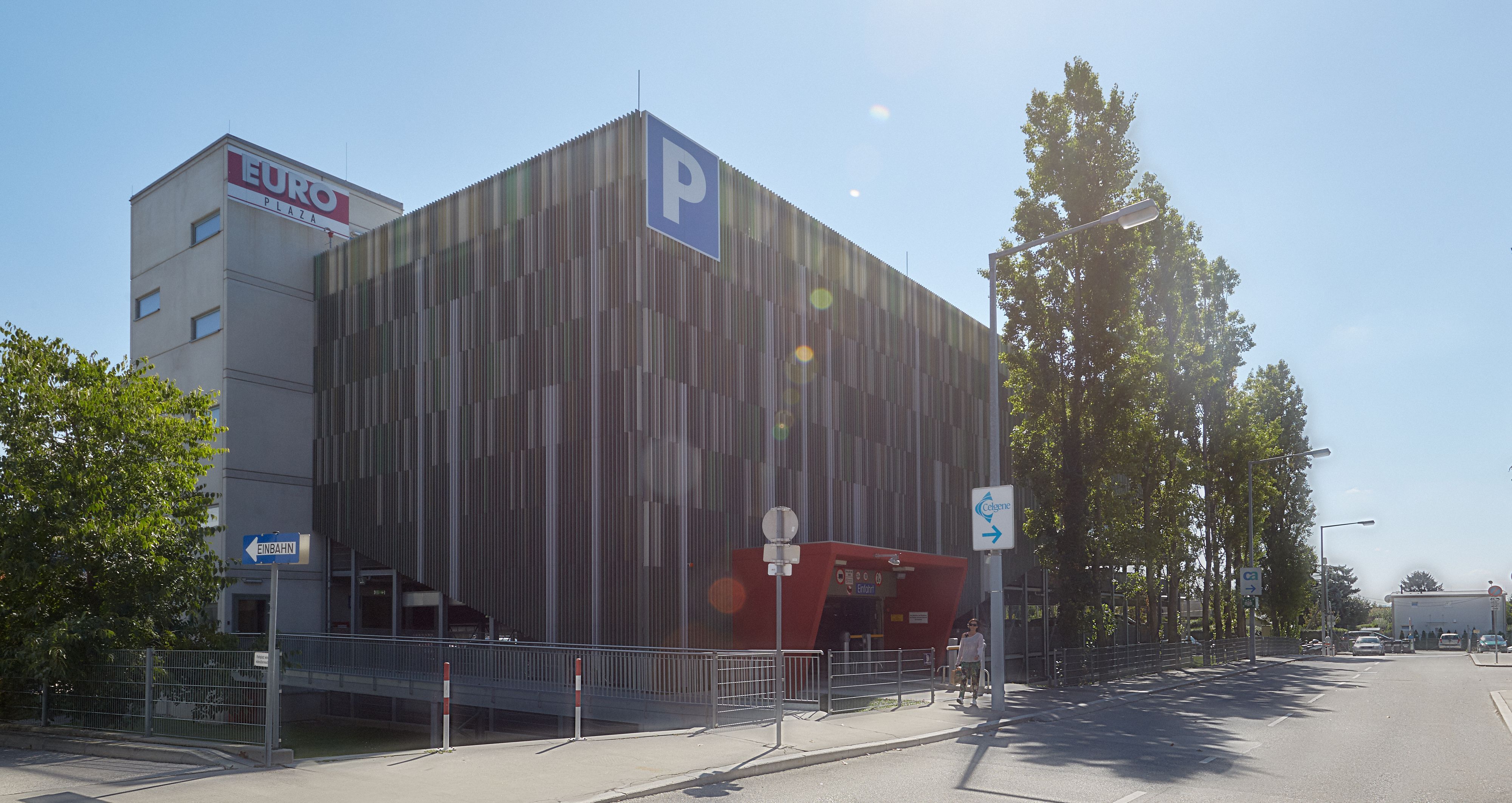 Foto: mehrgeschoßiges Parkhaus verdeckt hinter einer Fassade aus unzähligen vertikal ausgerichteten Paneelen; hochgewachsene Pappeln im Vordergrund 