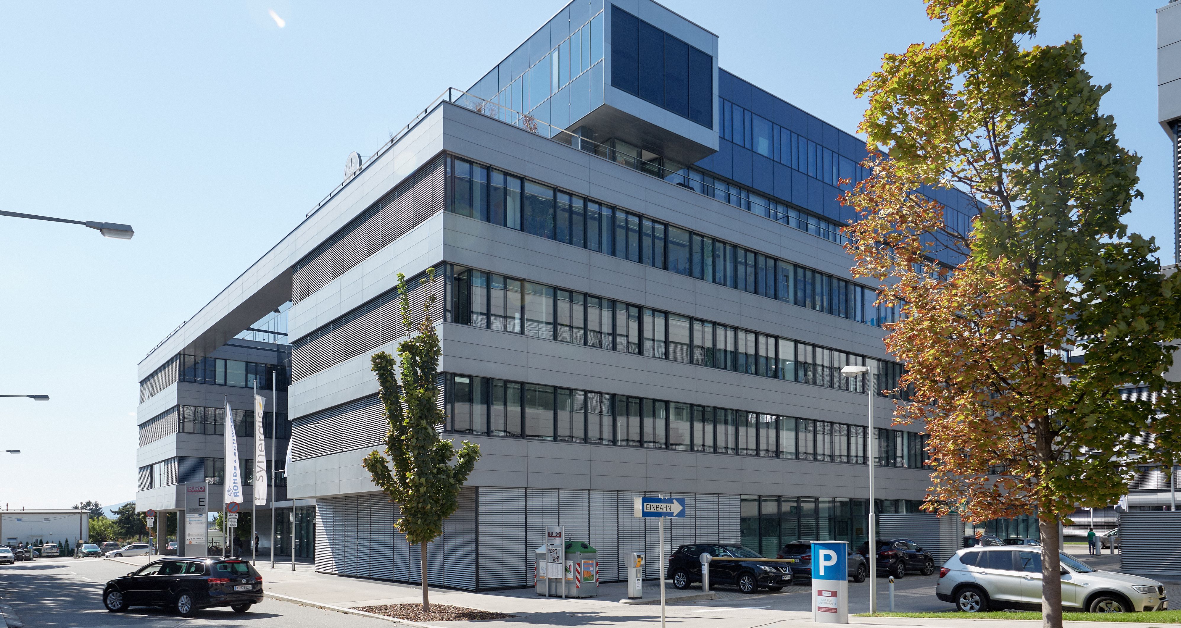 Foto: modernes Bürogebäude mit sechs Geschoßen und Alu-Glasfassade; in der Mitte des Bildes weist ein „Einbahn“-Schild in eine Einbahnstraße an der rechten Seite des Gebäudes 