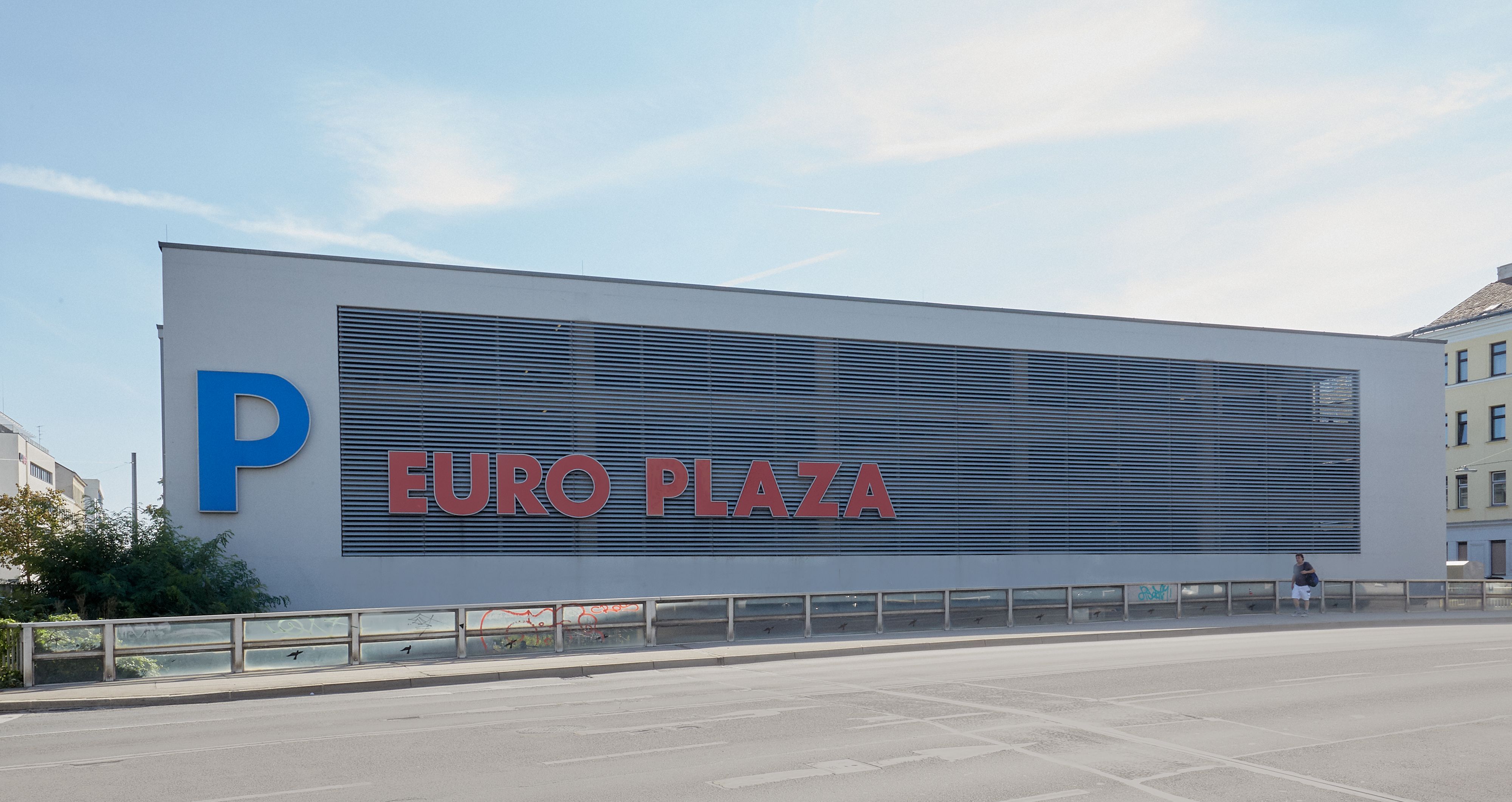 Foto: Längsseite eines Parkhauses mit teils transparenter Fassade; darauf eine dreidimensional gefertigte Aufschrift „P EURO PLAZA“; im Vordergrund eine leere mehrspurige Straße 