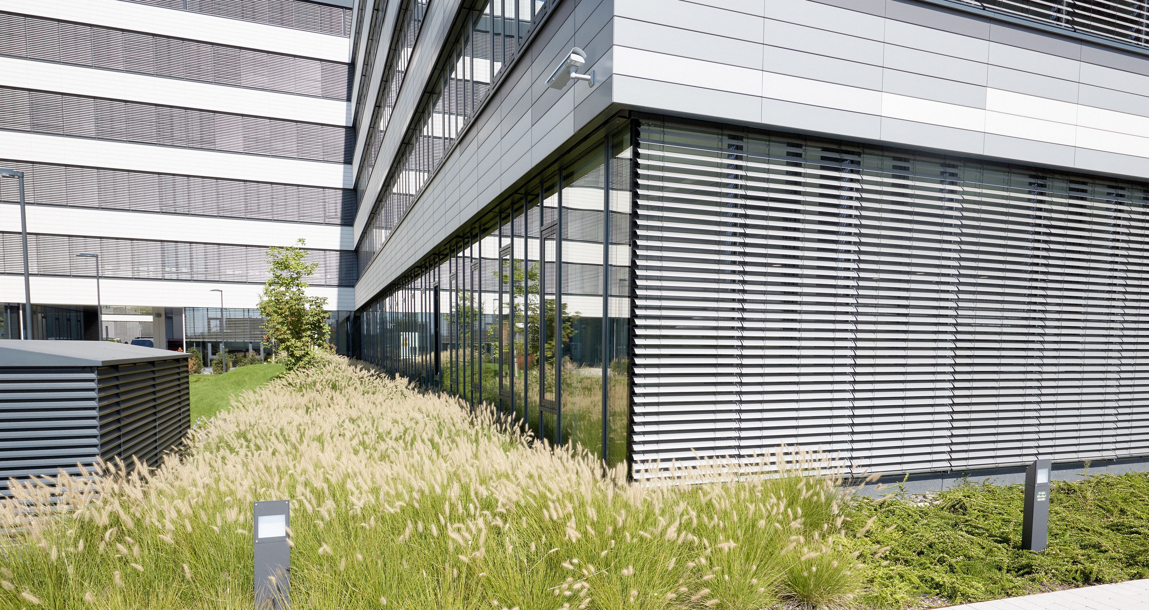 Foto: Kante eines hochmodernen Bürogebäudes mit Alu-Glas-Fassade und modern gestalteten Grünflächen