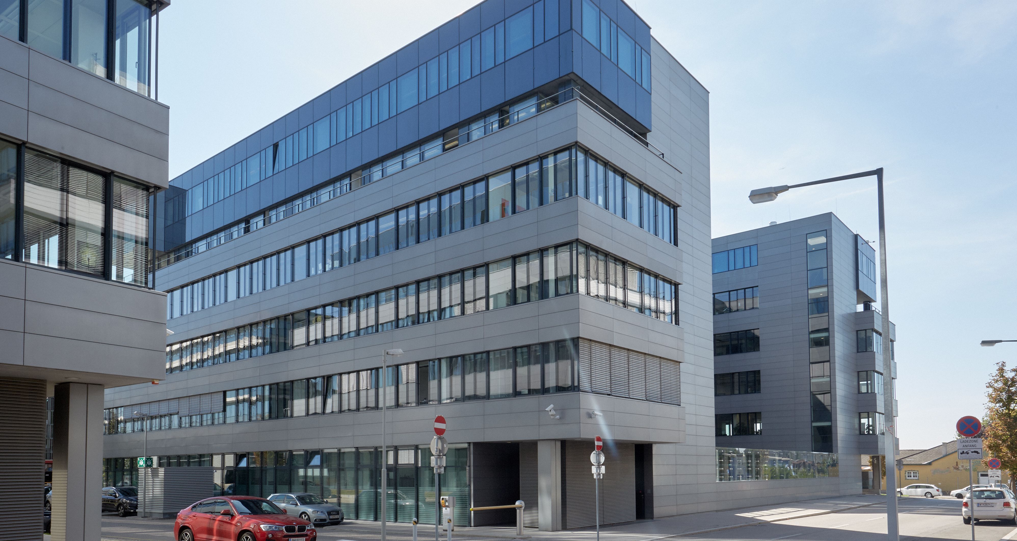 Foto: zwei moderne Bürogebäude mit jeweils sechs Geschoßen und Alu-Glasfassade schräg hintereinander, im Vordergrund wird ein drittes Bürogebäude angeschnitten