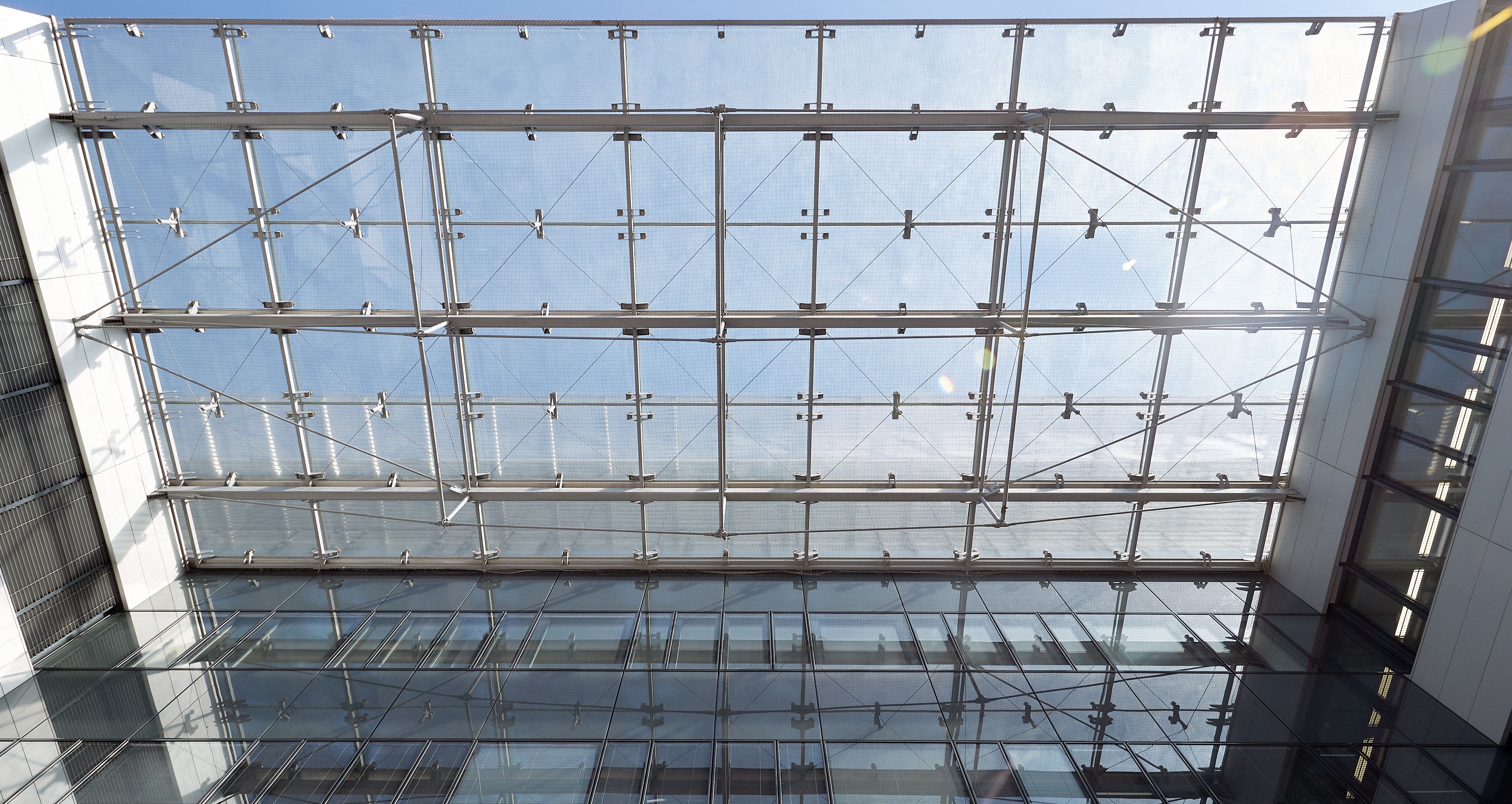 Foto: Blick von unten hinauf entlang der Alu-Glasfassade eines modernen Bürogebäudes; durch eine Alu-Glas-Überdachung sieht man den Himmel