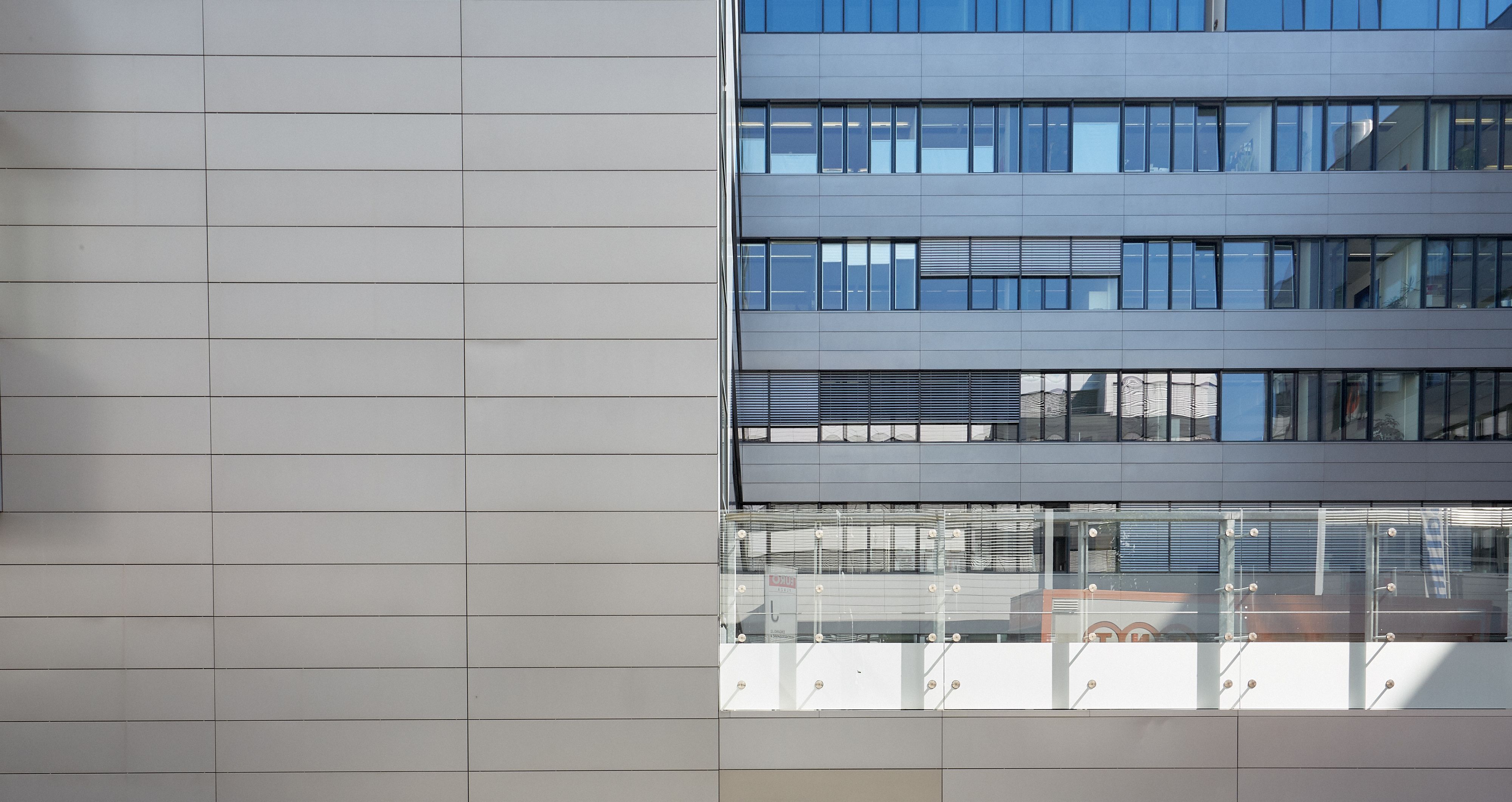 Foto: mehrere Fensterreihen eines modernen Bürogebäudes im Kontrast zu einer gekachelten Wand, die die linke Seite des Bildes einnimmt  